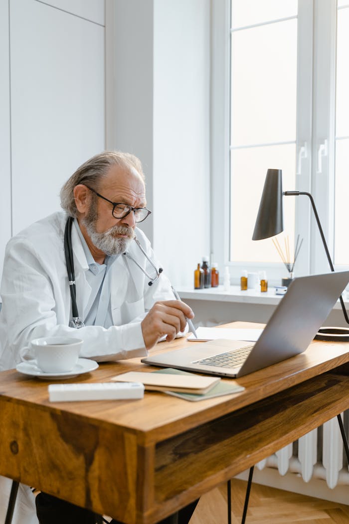 services-02 Elderly doctor in office using laptop for telemedicine consultation, showcasing modern healthcare tech.